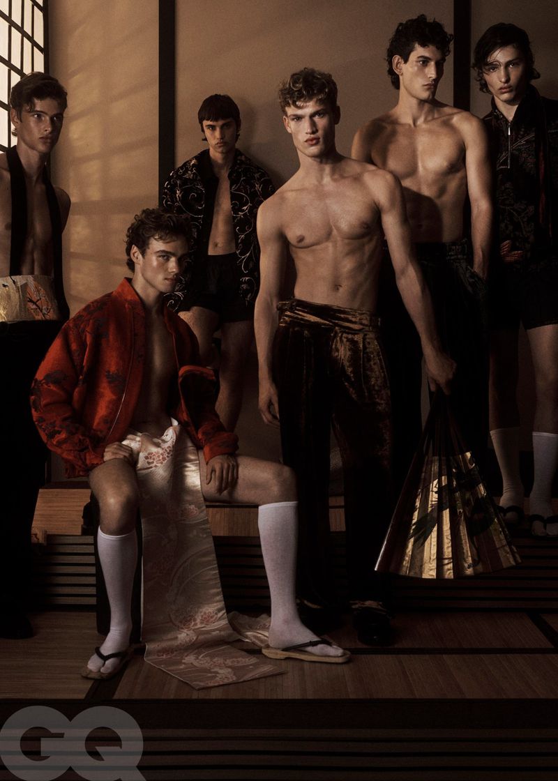 Group of six young adult male fashion models in traditional Japanese-inspired clothing posing indoors, warm lighting, GQ magazine logo.