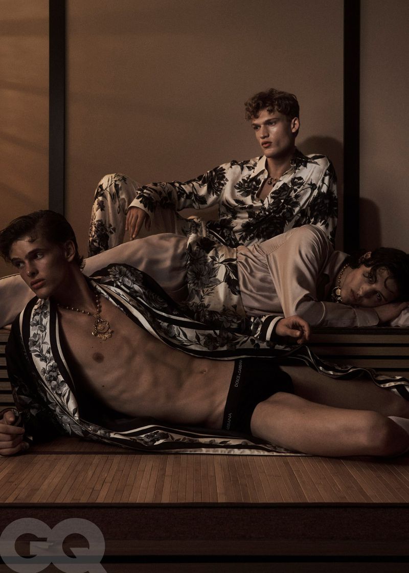 Three men lounge indoors wearing floral patterned sleepwear and gold necklaces in a fashion editorial, lit with soft, diffused light.