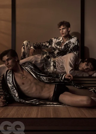 Three men lounge indoors wearing floral patterned sleepwear and gold necklaces in a fashion editorial, lit with soft, diffused light.