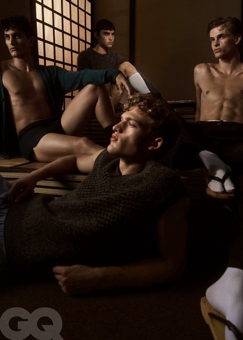 Group of four young adult men in a fashion editorial, posing indoors in casual attire, warm color grading, medium shot.