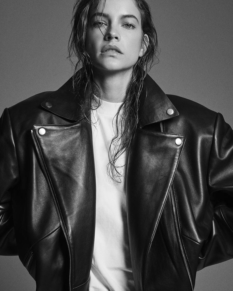 Barbara Palvin wearing an oversized black leather biker jacket and white t-shirt against a grey studio backdrop.
