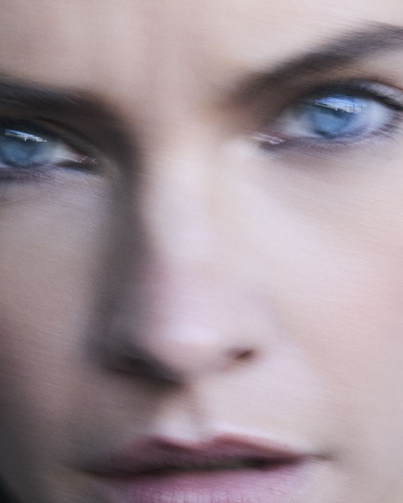 Extreme close-up on a woman's face, featuring her blue eyes, nose, and lips in soft focus, giving an ethereal and intimate feel.