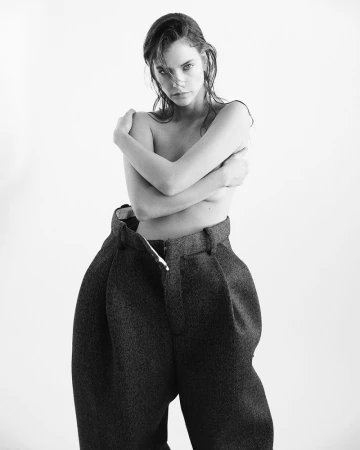 Barbara Palvin posing topless in oversized high-waisted dark wool trousers against a white seamless studio backdrop.