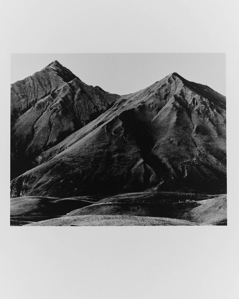 Monochrome landscape photograph of rolling hills and peaks of a mountain range under a clear sky. Serene nature photography.