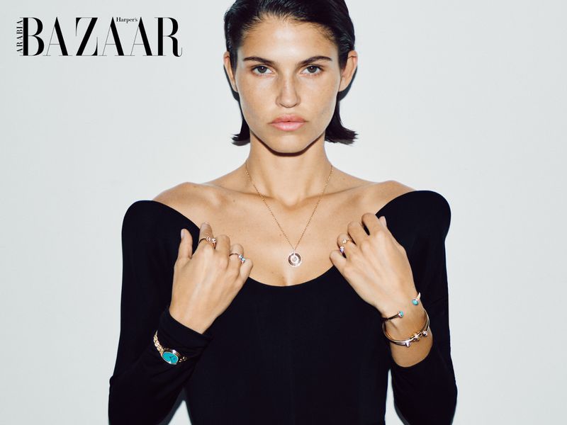 Model Julieta Gracia wearing an off-shoulder black top and fine gold jewelry against a white studio background.