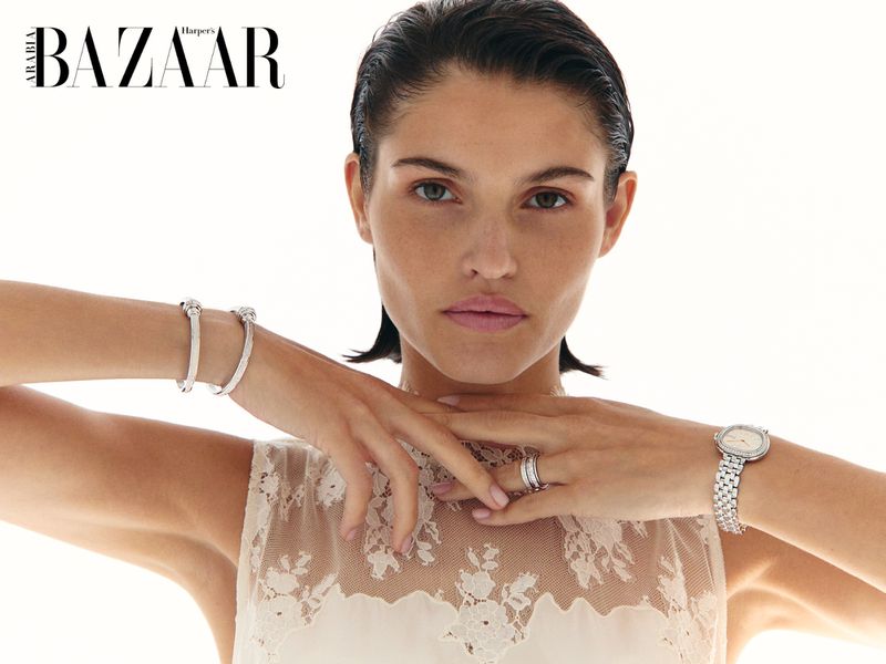 Model Julieta Gracia posing in a sheer lace top and silver jewelry against a white studio backdrop for Harper's Bazaar Arabia.