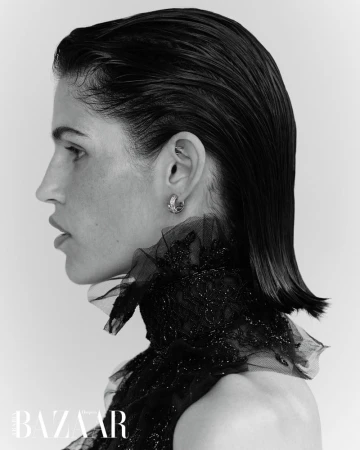 Monochromatic portrait of a woman with wet-look hair, wearing an elegant black lace high-neck dress, earring, and a neutral background.