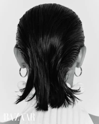 Close-up view from behind of slicked-back wet hair and silver hoop earrings against a white studio background.