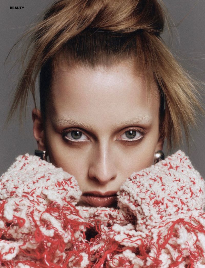 Close-up beauty shot of a fair-skinned woman with white eyeliner and pale eyebrows, wearing a textured red and white scarf.