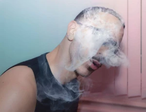 Man wearing a black tank top with smoke swirling around his face against a pastel background for Double Magazine.