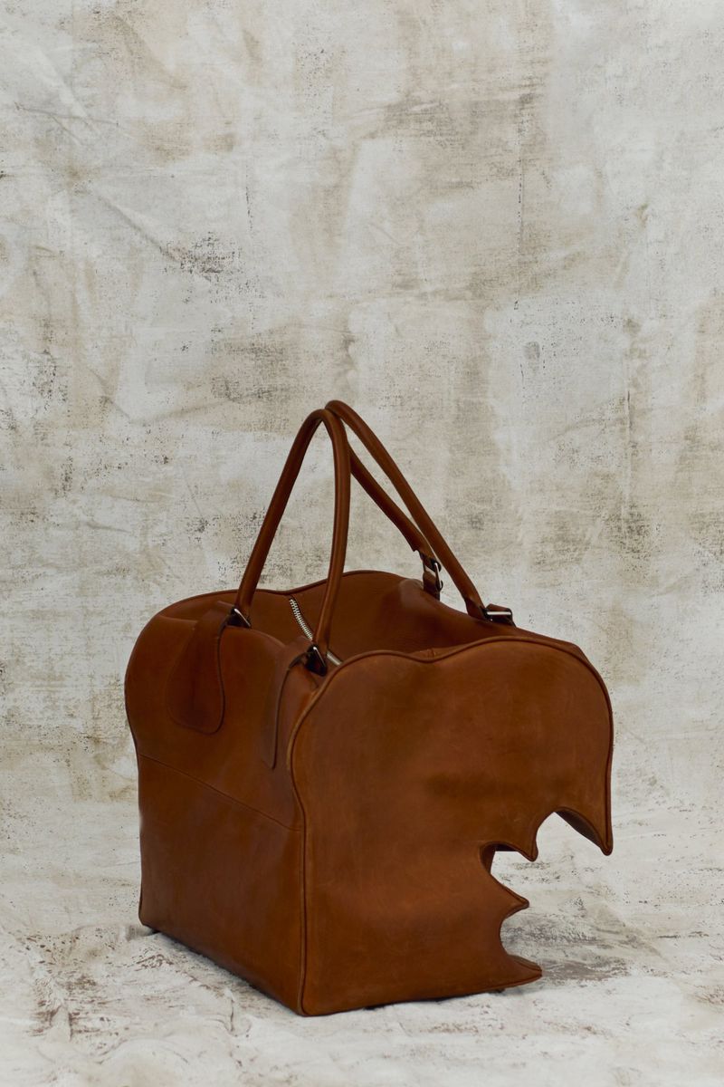 Brown leather duffel bag featuring a unique, artistic design, placed in a neutral studio setting. Focus on texture and craftsmanship.