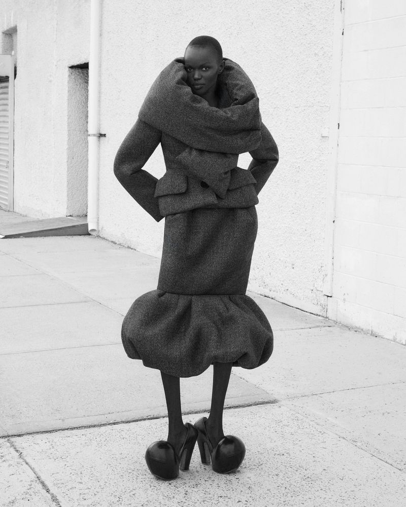 Striking black and white fashion shot of an African woman in an avant-garde jacket, skirt, and heels in an outdoor urban setting.
