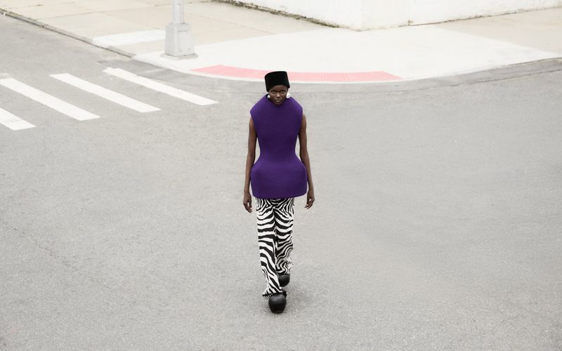 Woman in purple top and zebra pants walks on crosswalk with urban background in fashion shot, high angle, studio-lit.