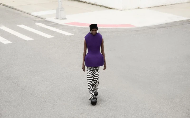 Woman in purple top and zebra pants walks on crosswalk with urban background in fashion shot, high angle, studio-lit.