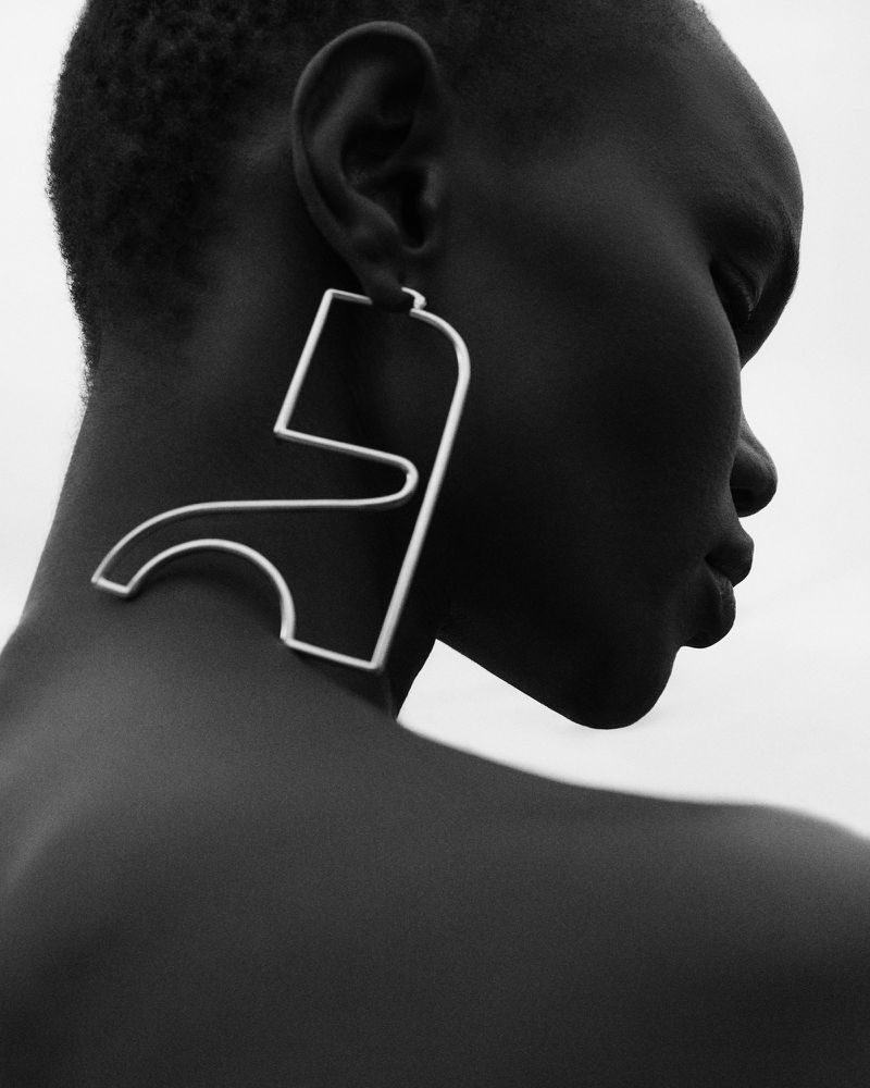 Profile of an adult female wearing an avant-garde geometric earring in a studio shot with a monochromatic color palette.