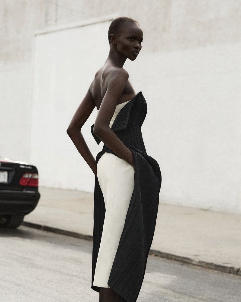 Elegant Black woman poses in a high fashion black and white strapless dress on a street with a car parked in the background.