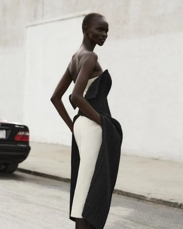 Elegant Black woman poses in a high fashion black and white strapless dress on a street with a car parked in the background.