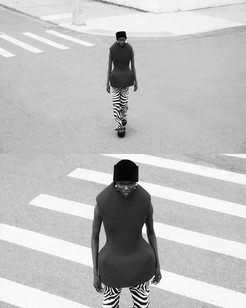 Fashion shot in black and white featuring an African woman in a sculptural top and zebra-print pants crossing the street on a crosswalk.