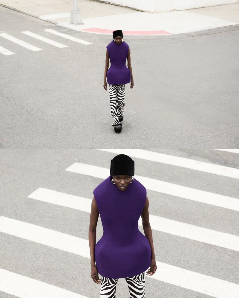 Fashionable woman in a purple top and zebra-print pants confidently strides across a crosswalk on a sunny urban street.
