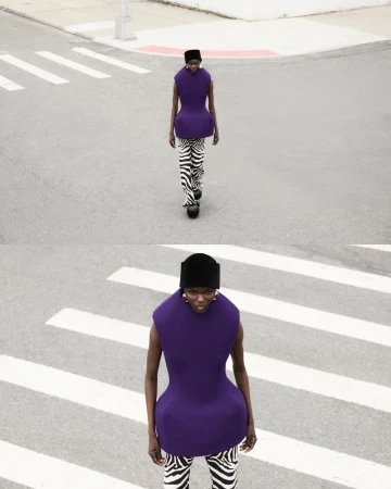 Fashionable woman in a purple top and zebra-print pants confidently strides across a crosswalk on a sunny urban street.