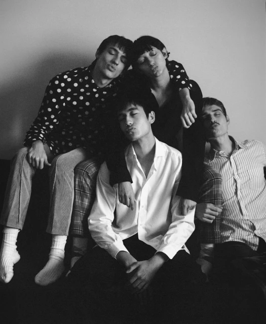 Black-and-white portrait of four men in patterned shirts posing indoors with neutral expressions, creating an understated yet intriguing composition.