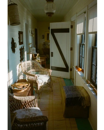 A sunlit indoor porch with wicker furniture, patterned flooring, and bright natural light filtering through the windows creating a cozy interior.
