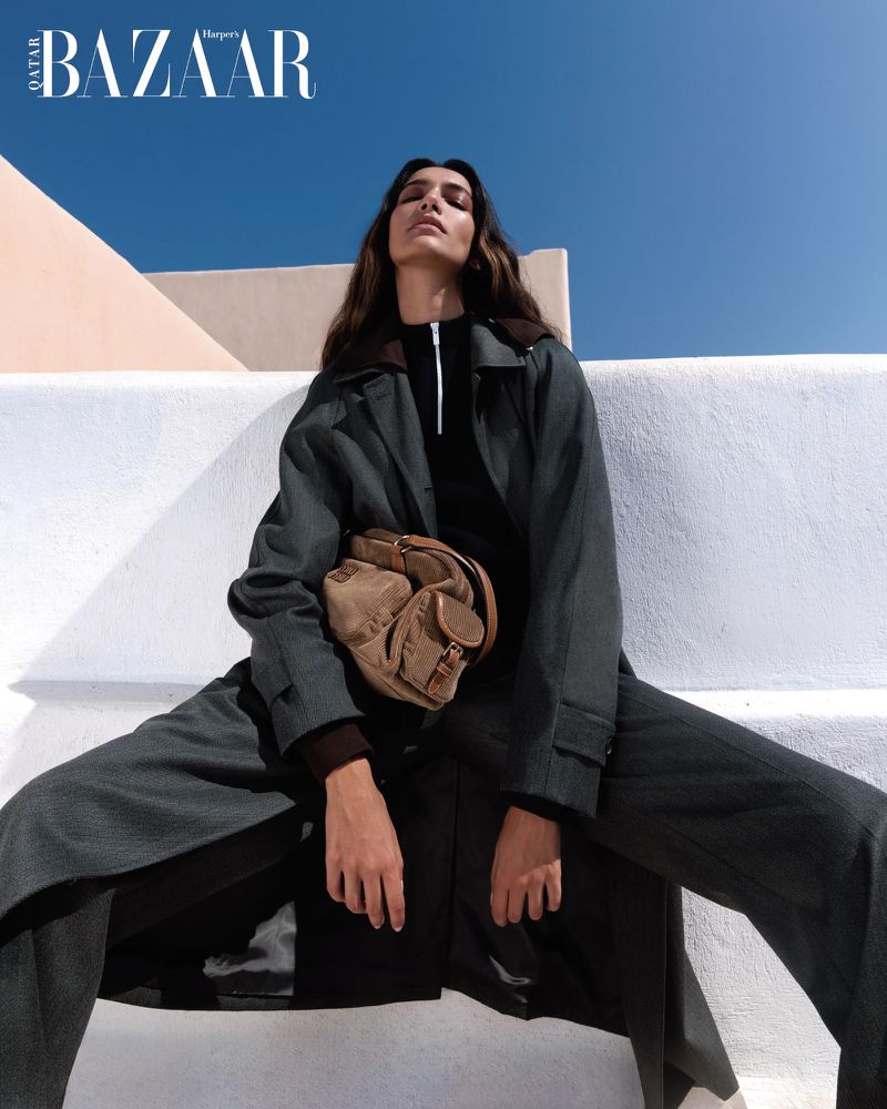 A woman in a coat poses on a whitewashed rooftop with a blue sky backdrop, promoting fashion in an outdoor editorial shot.