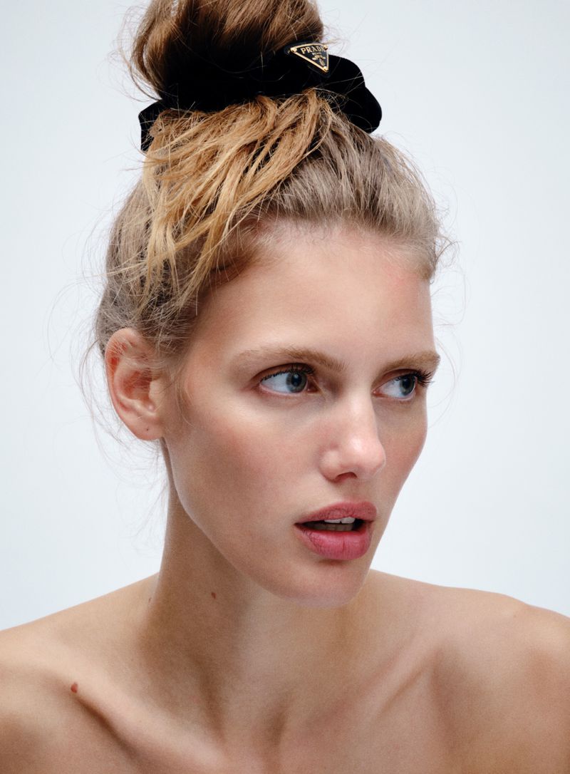 Close-up studio shot of a fair-skinned young adult woman wearing a black velvet Prada scrunchie in a high bun. Clean, white background.