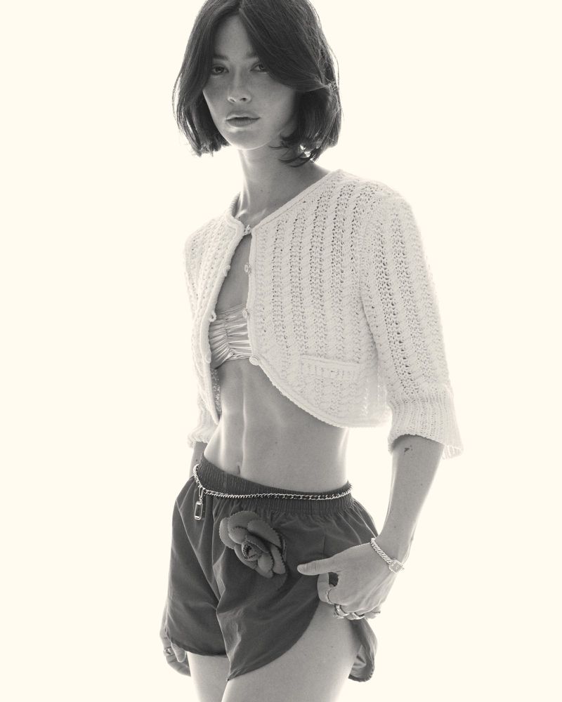 Monochrome portrait of an athletic woman in a crocheted cardigan and shorts with a rose detail, looking directly at the camera.