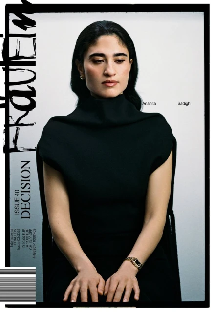 Editorial fashion shot: a woman wearing a black dress and gold watch sits in front of a white background, portrait framed by a magazine cover.