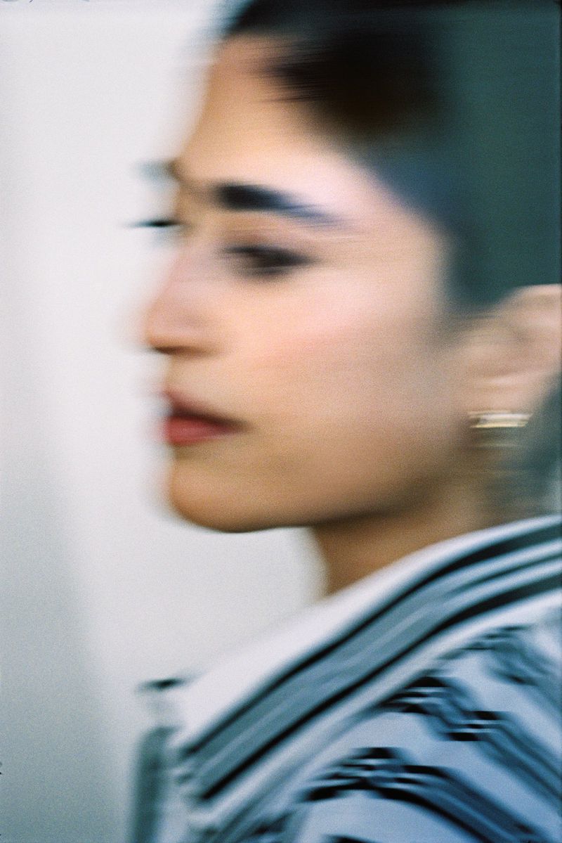 Motion-blurred profile close-up portrait of a woman wearing a patterned collared top and small gold earring.