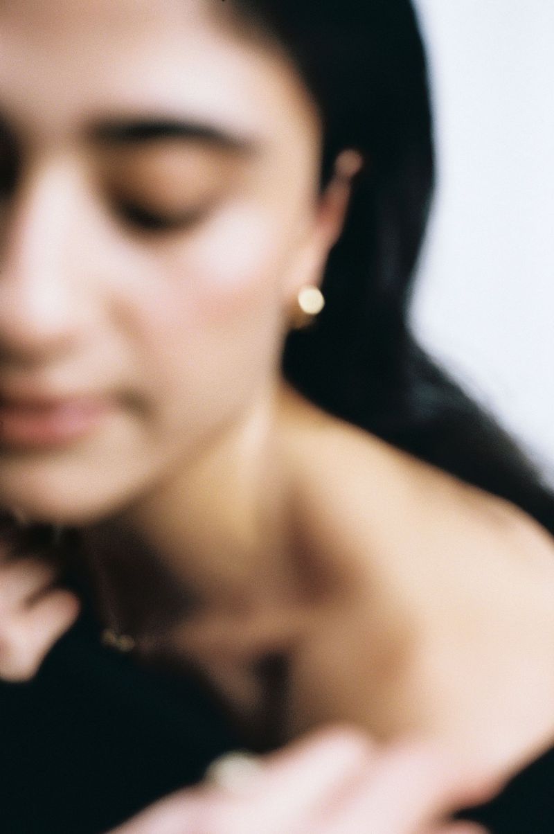 Close-up portrait of a woman with dark hair and gold hoop earrings against a light background, softly out of focus.