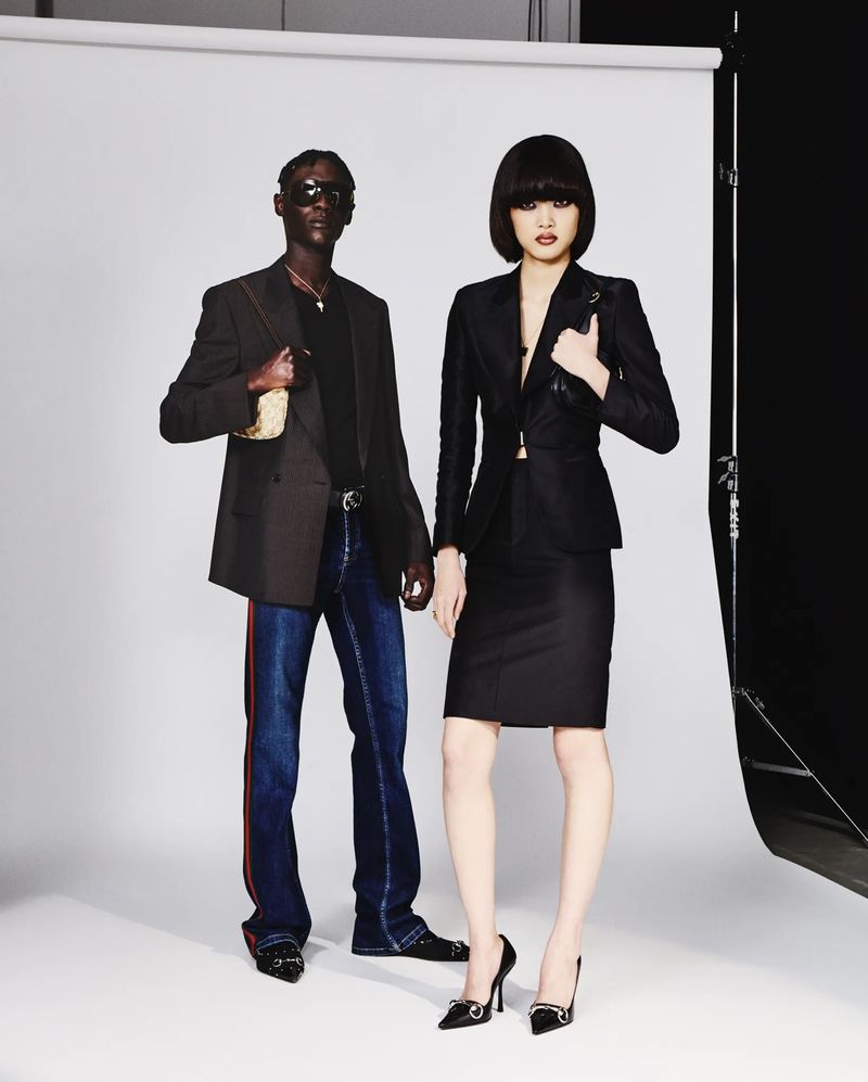 A stylishly dressed couple poses in a photo studio, showcasing modern business attire with blazers, skirts, and dark jeans.