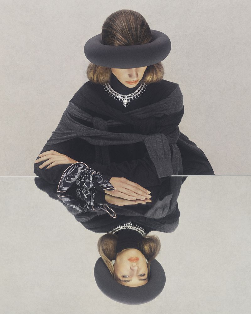 Woman in a black hat and clothes with a mirrored reflection, against a neutral background. Fashion and portrait photography.