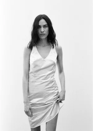 Alexa Chung posing in a sleeveless white satin slip dress against a plain studio background.