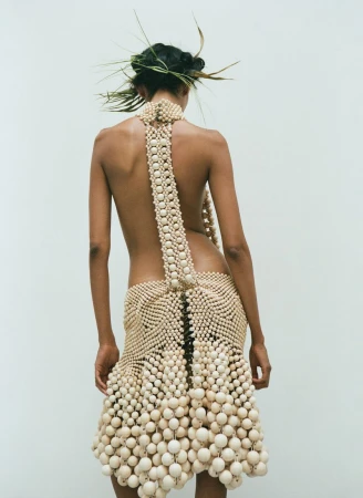Back view of an adult woman in a beaded dress with matching beaded strap, accessorized with spiky headpiece, against a white backdrop.