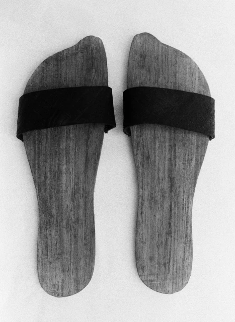 Close-up of pair of wooden Japanese geta sandals with black straps on a white surface, highlighting craftsmanship and minimalistic design.