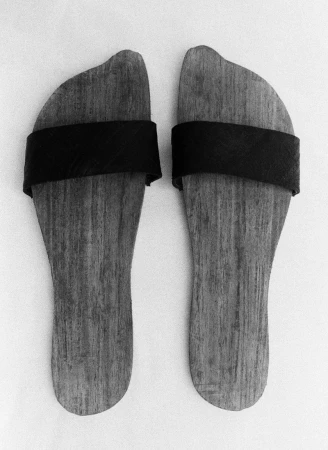 Close-up of pair of wooden Japanese geta sandals with black straps on a white surface, highlighting craftsmanship and minimalistic design.