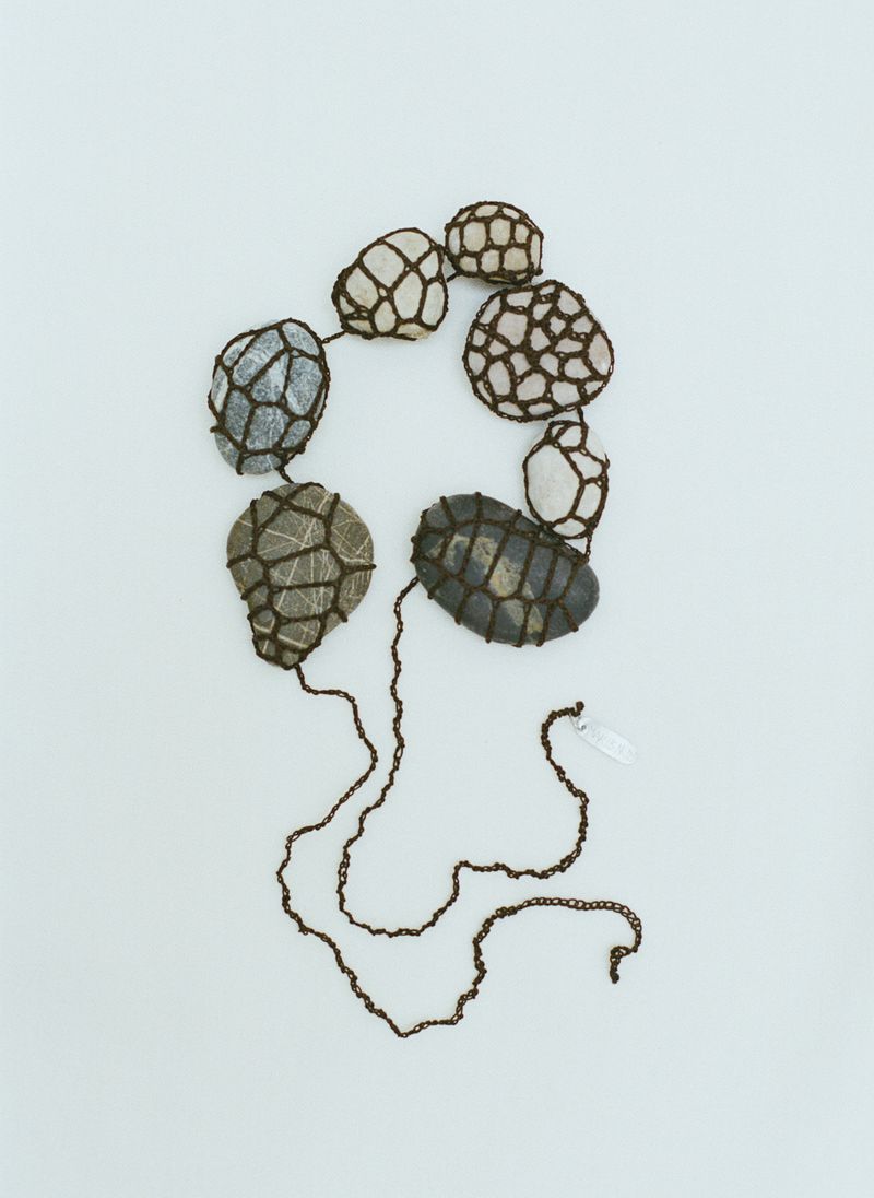 Necklace featuring a unique design with various rocks held together by a woven brown cord against a light background.