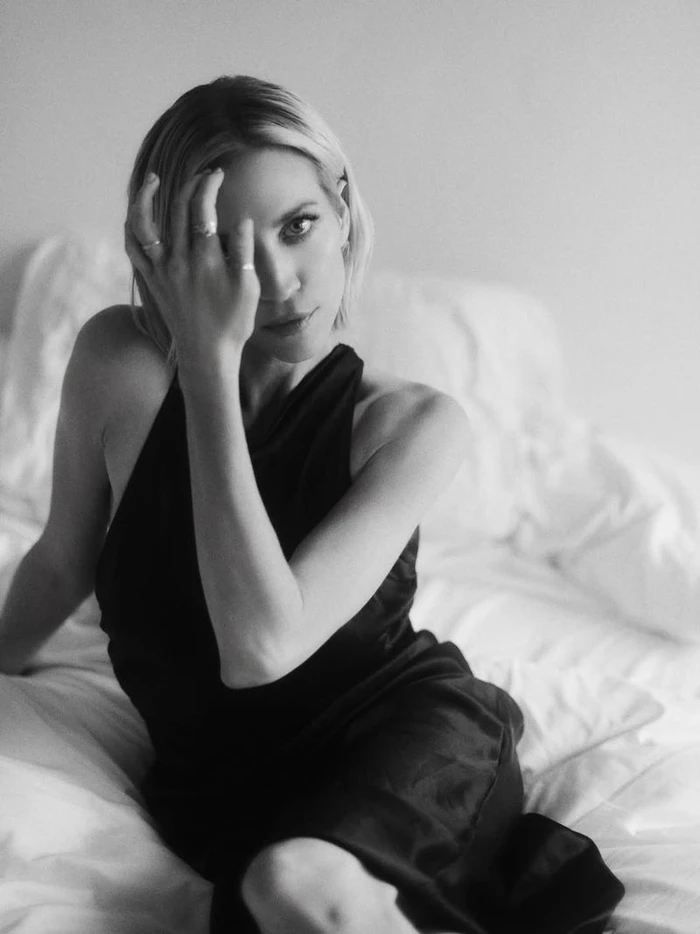 Portrait of Brittany Snow in a black dress sitting on a white bed for Town and Country photographed by Lauren Withrow