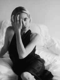 Portrait of Brittany Snow in a black dress sitting on a white bed for Town and Country photographed by Lauren Withrow