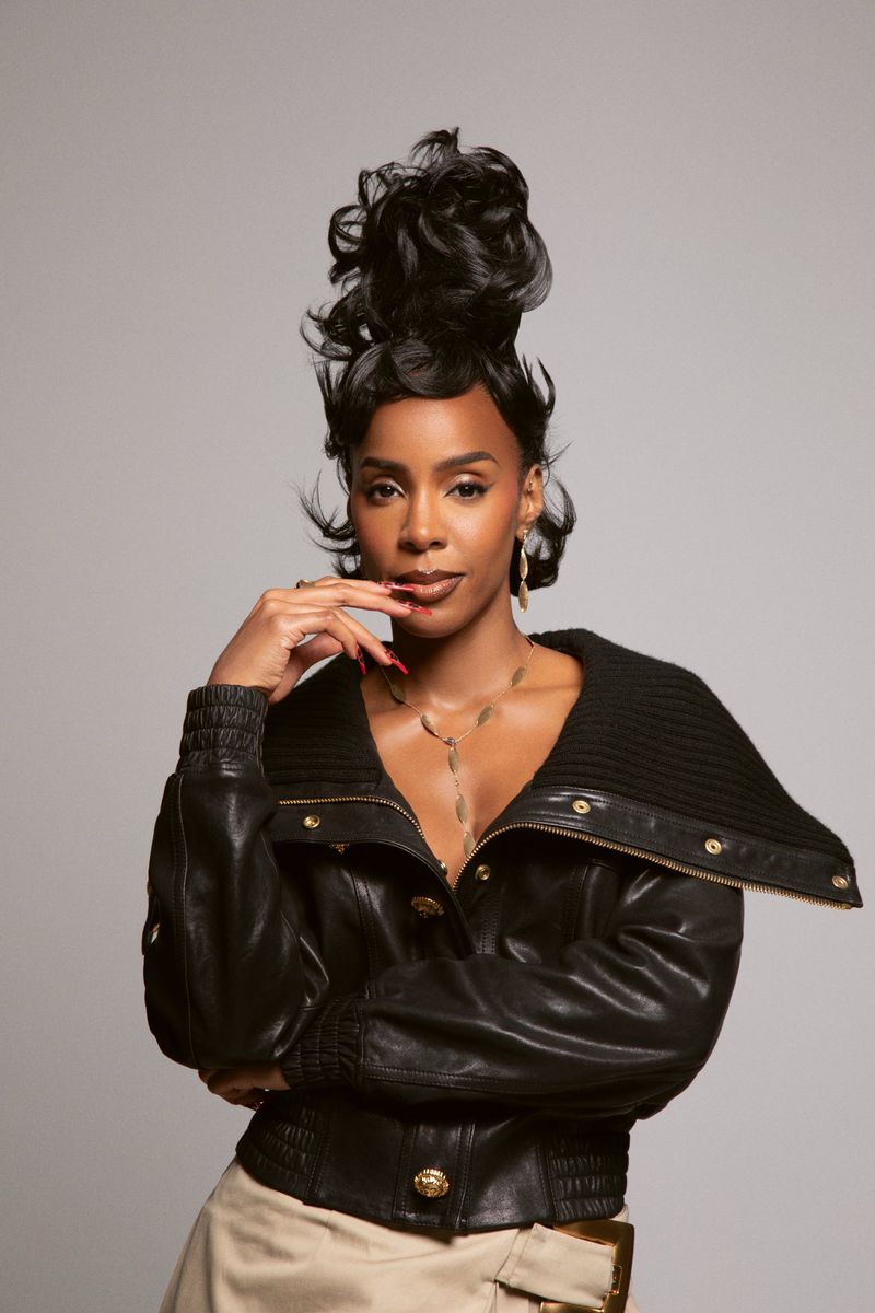 Portrait of a beautiful adult woman with dark hair in a black leather jacket against a plain gray studio backdrop.