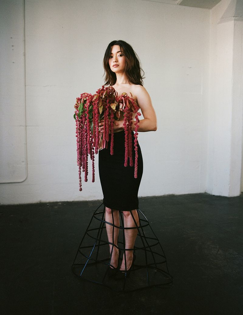 Woman in black dress with floral installation, posing in bright studio, creating unique and fashion-forward portrait.