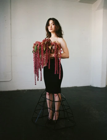 Woman in black dress with floral installation, posing in bright studio, creating unique and fashion-forward portrait.