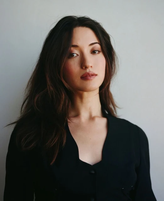 Portrait of a woman with long dark hair, wearing a black top, looking directly at the camera against a neutral background.