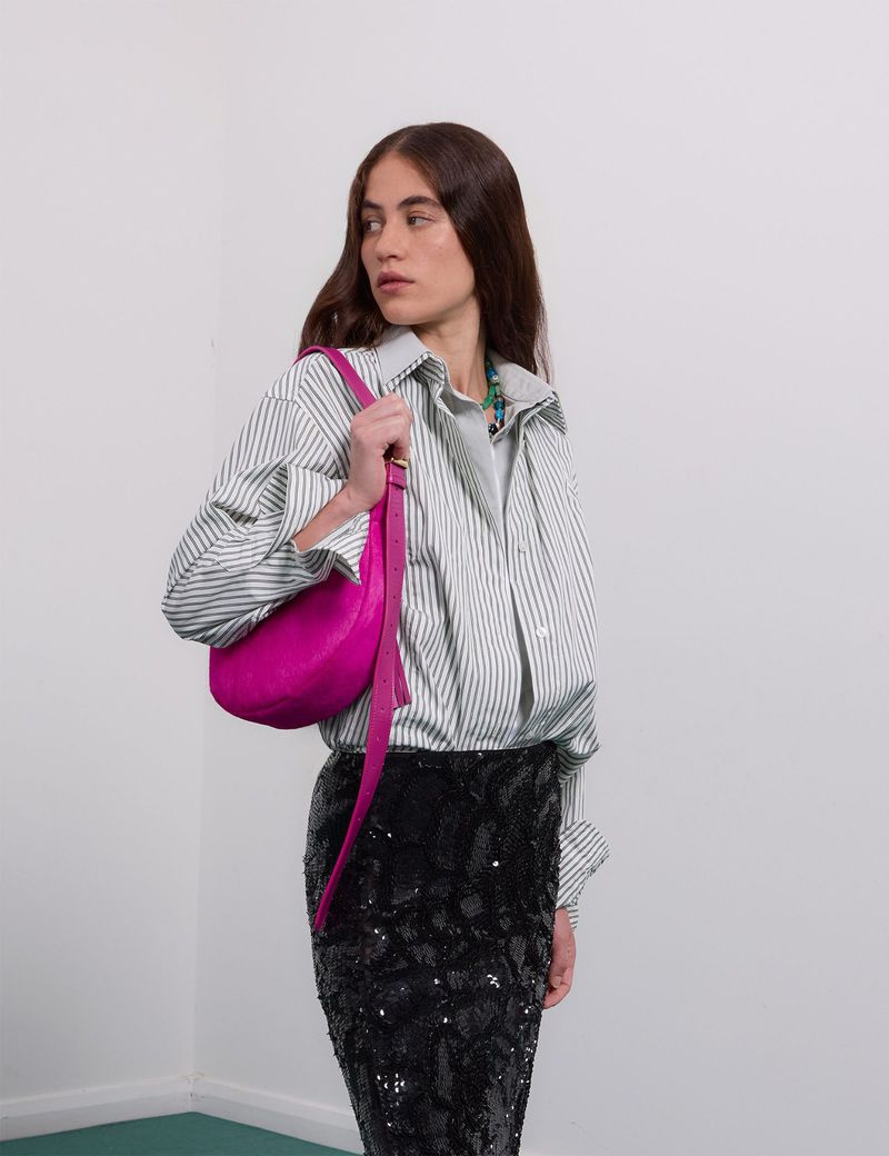 Adult female with long brunette hair wearing a striped button-down shirt and a black sequin skirt, carrying a bright pink handbag.