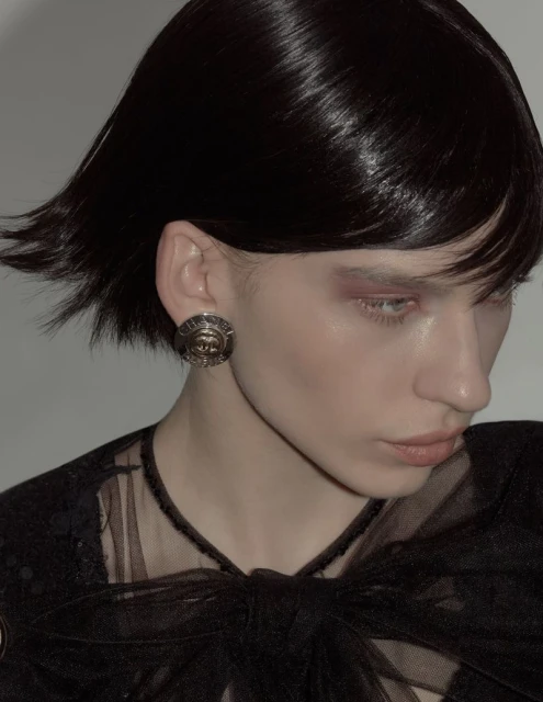 Close-up of a female model with dark hair and an earring, wearing a black lace top, against a neutral grey backdrop in a photo studio.