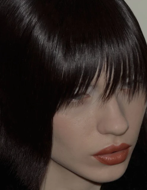 Close-up of a woman with dark brown hair and blunt bangs, shiny lips, and fair skin, set against a soft white background. Beauty shot.