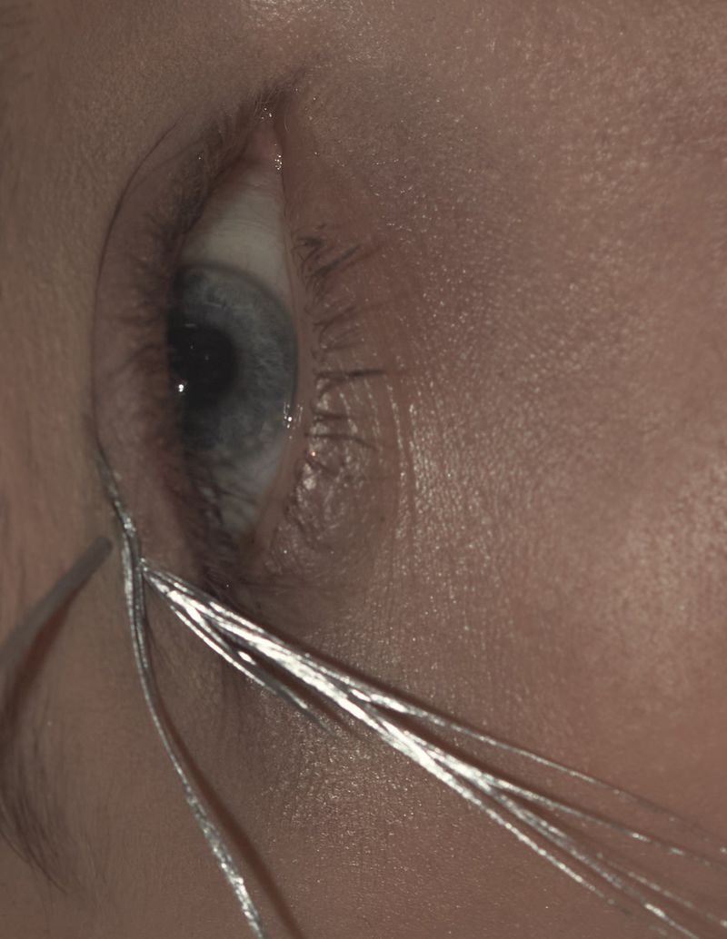 Macro shot of a human eye with blue iris and shiny silver tinsel, capturing the details of the skin texture and eyelashes.
