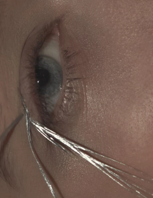Macro shot of a human eye with blue iris and shiny silver tinsel, capturing the details of the skin texture and eyelashes.
